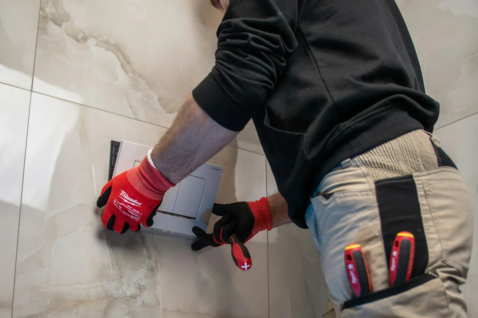Plumber in work gloves fitting the frame for a wall-hung toilet